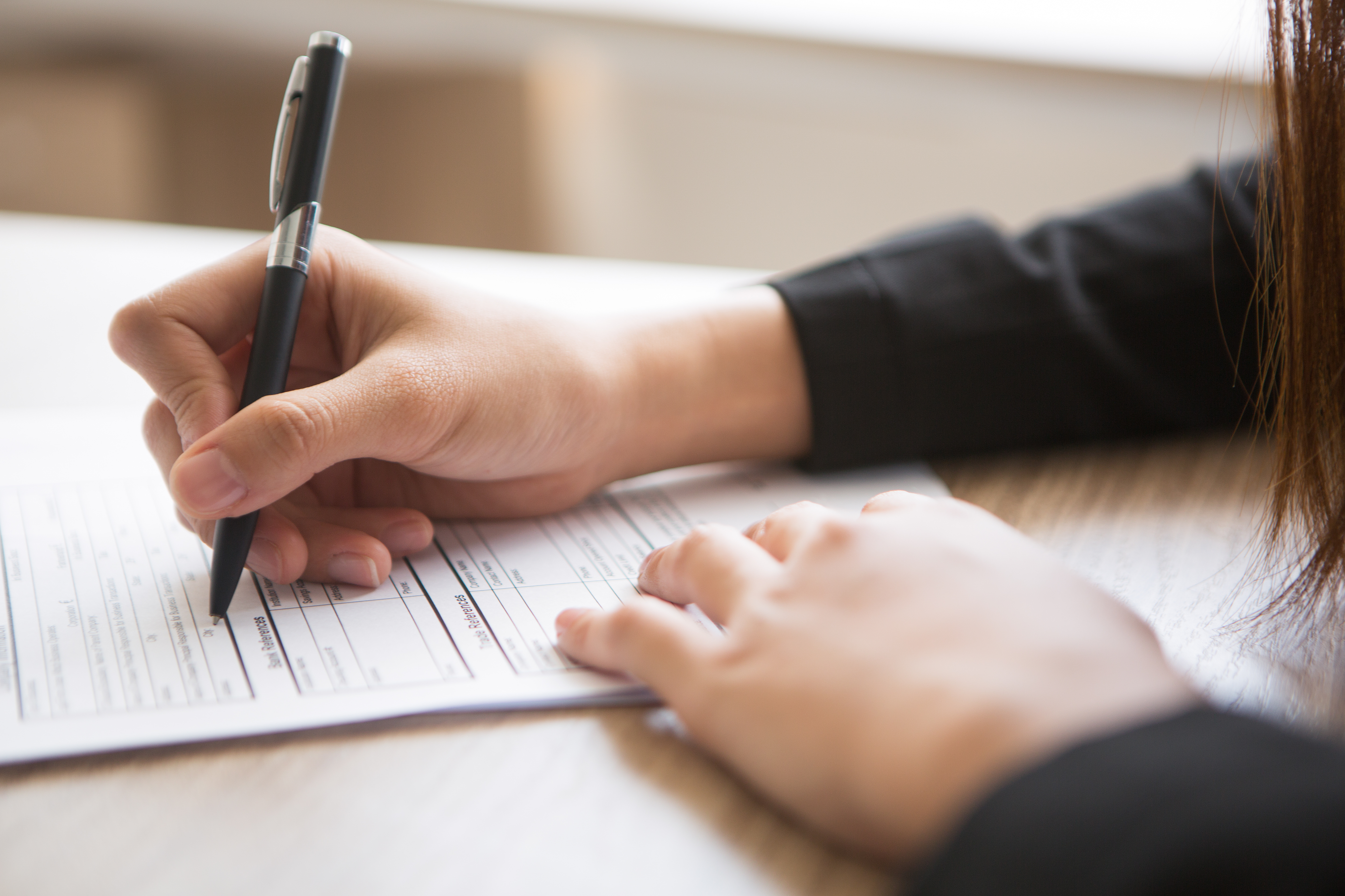 Une main remplissant un document, symbole du travail de fond mené avec le réseau de partenaires de confiance de l’agence Thomas d’Aquin