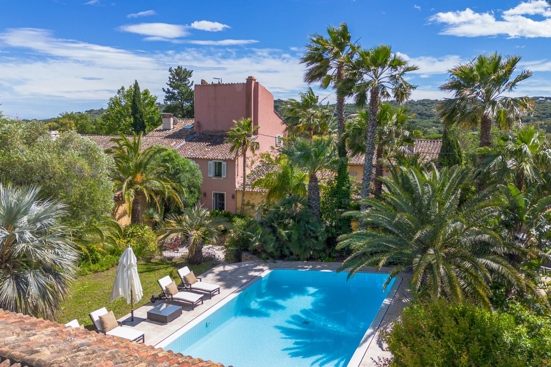 Veduta aerea di una lussuosa villa privata con piscina a sfioro affacciata sulla costa di Pampelonne, vicino a Saint-Tropez, circondata da pini e macchia mediterranea, in una limpida giornata estiva.